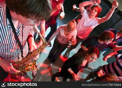 Saxophonist playing in a nightclub, with dancing people in the background