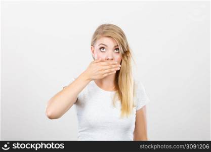 Saying bad things, shocking news concept. Ashamed young blonde woman having hand on her mouth. Studio shot on grey background.. Ashamed woman having hand on mouth