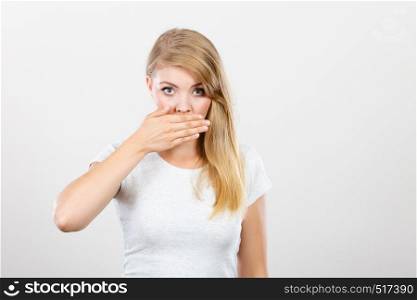 Saying bad things, shocking news concept. Ashamed young blonde woman having hand on her mouth. Studio shot on grey background.. Ashamed woman having hand on mouth