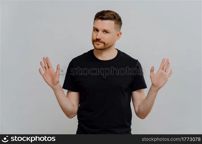 Saying no. Young bearded man in black tshirt demonstrating refusal sign or stop gesture, asking not to bother him while standing against grey background in studio. Denial concept. Young handsome male in casual t shirt saying no or rejecting proposition
