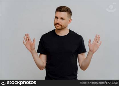 Saying no. Young bearded man in black tshirt demonstrating refusal sign or stop gesture, asking not to bother him while standing against grey background in studio. Denial concept. Young handsome male in casual t shirt saying no or rejecting proposition
