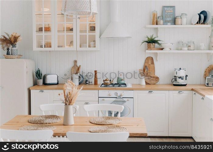 Scandinavian kitchen design. Modern apartment decoration. Domestic kitchen or dining room. White luxurious interior lit by daylight. Kitchen appliance, utensils, stove, table and refrigerator.. Scandinavian kitchen design. Modern dining room decoration. White luxurious interior and appliance.