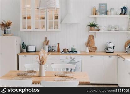 Scandinavian kitchen design. Modern apartment decoration. Domestic kitchen or dining room. White luxurious interior lit by daylight. Kitchen appliance, utensils, stove, table and refrigerator.. Scandinavian kitchen design. Modern dining room decoration. White luxurious interior and appliance.