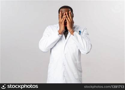 Scared, insecure and shocked african-american male doctor, physician cant look at severe trauma of patient, close eyes and peeking through fingers with frightened, horrified expression.. Scared, insecure and shocked african-american male doctor, physician cant look at severe trauma of patient, close eyes and peeking through fingers with frightened, horrified expression