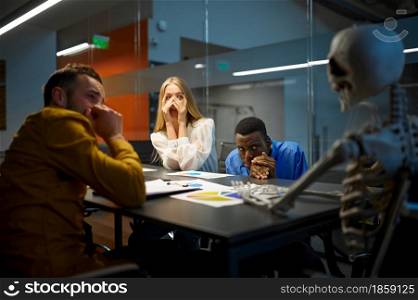 Scared managers and skeleton, conference in IT office, joke. Professional teamwork and planning, group brainstorming and corporate work, meeting of colleagues. Scared managers and skeleton in IT office, joke