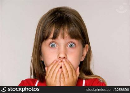 Scared six year old girl with hands covering mouth.
