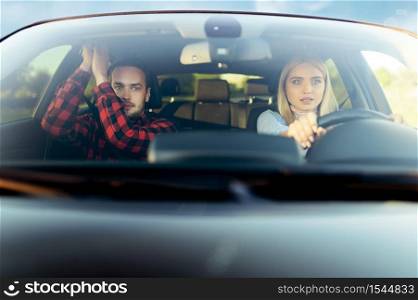 Scared woman and instructor in car, front view, driving school. Man teaching lady to drive vehicle. Driver&rsquo;s license education, an accident. Scared woman and instructor in car, front view