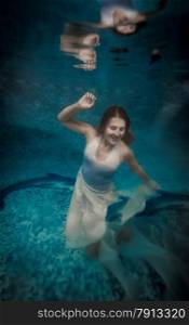 Scared woman in long white dress drowning at deep swimming pool