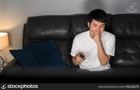 scared young man is watching horror movie TV on sofa at night