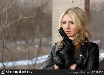 Scared young woman in leather jacket with a gun