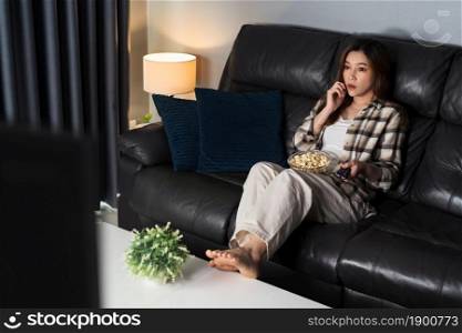 scared young woman is watching horror movie TV on sofa at night