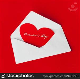 Scarlet heart in a white envelope on the red background