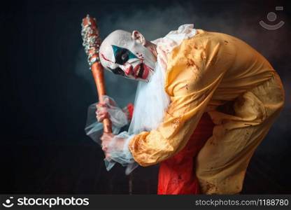 Scary bloody clown with crazy eyes holds baseball bat. Man with makeup in carnival costume, mad maniac. Bloody clown with crazy eyes holds baseball bat