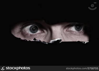 Scary eyes of a man spying through a hole in the wall