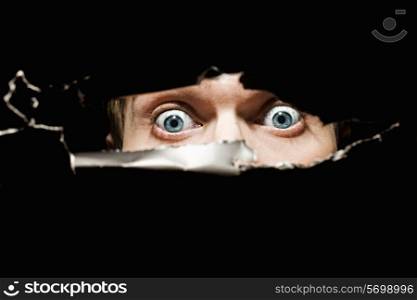 Scary eyes of a man spying through a hole in the wall close up