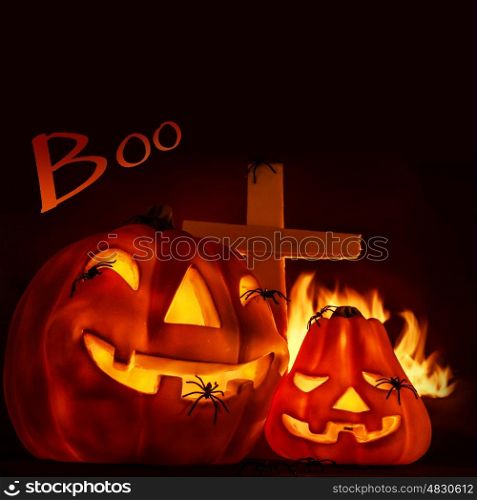 Scary Halloween night, aggresive burning fire on graveyard near cross, glowing gourd with creepy spiders, copyspace with text, traditional autumn holiday of horror