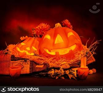 Scary Halloween still life on dark red background, creepy carved glowing pumpkin with spiders and dry flowers, frightening party decoration