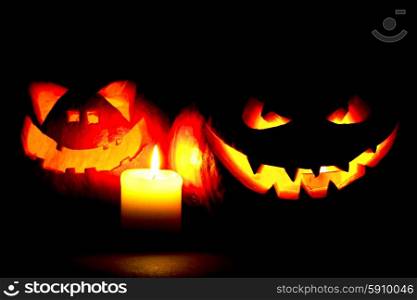 Scary smiling Halloween pumpkins and candle on dark background. Halloween pumpkins