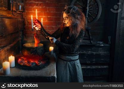 Scary witch cooking soup with human body parts, dark powers of witchcraft, spiritual seance with candles. Female foreteller calls the spirits, terrible future teller. Scary witch cooking soup with human body parts