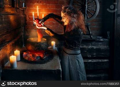 Scary witch cooking soup with human body parts, dark powers of witchcraft, spiritual seance with candles. Female foreteller calls the spirits, terrible future teller