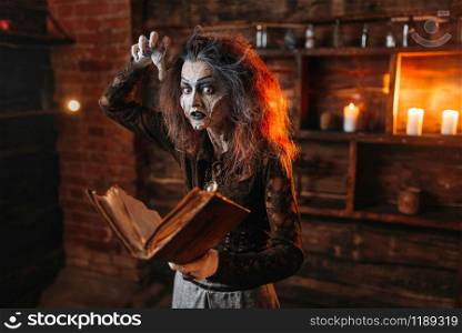 Scary witch holds spellbook, dark powers of witchcraft, spiritual seance. Female foreteller calls the spirits, terrible future teller. Witch holds spellbook, dark powers of witchcraft