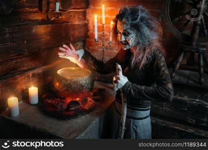 Scary witch reads spell over the pot, dark powers of witchcraft, spiritual seance with candles. Female foreteller calls the spirits, terrible future teller. Scary witch reads spell over the pot, seance