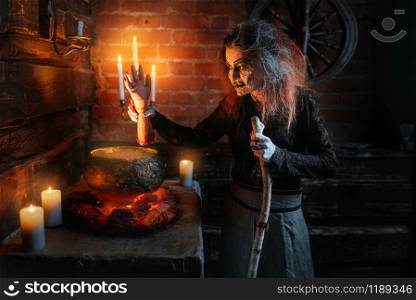 Scary witch reads spell over the pot with human body parts, dark powers of witchcraft, spiritual seance with candles. Female foreteller calls the spirits, terrible future teller. Witch reads spell over pot with human body parts