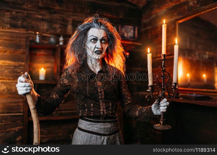 Scary witch with a candlestick and a cane reads mystic spell, spiritual seance. Female foreteller calls the spirits, terrible fortune teller