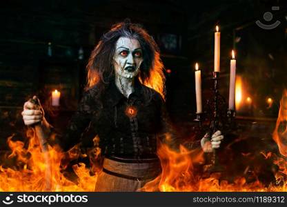 Scary witch with a cane at the mirror and candles, dark powers of witchcraft, spiritual seance. Female foreteller calls the spirits, terrible fortune teller. Scary witch with a cane at the mirror and candles