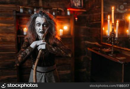 Scary witch with a cane at the mirror and candles, dark powers of witchcraft, spiritual seance. Female foreteller calls the spirits. Scary witch with a cane at the mirror and candles