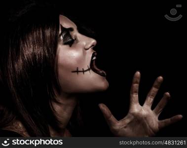 Scary witch yelling, side view of aggresive woman with painted face on black background, terrible grimace, Halloween party concept