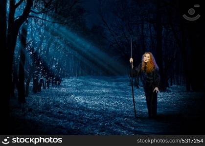 Scary young witch in night forest