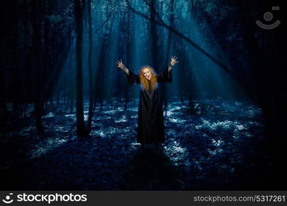 Scary young witch in night forest