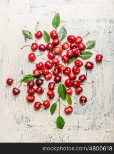 Scattered cherry berries with green leaves on light rustic background, top view. Summer fruit concept