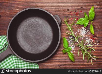 Scattered fresh basil and rosemary, sea salt and dry peppercorns near the frying pan