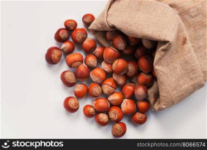 Scattered out of the bag unshelled hazelnuts on white background.. Unshelled hazelnuts in a bag on a white background. Not isolated