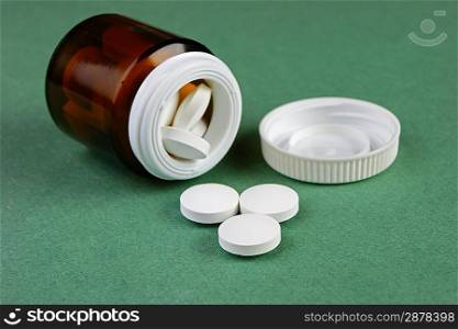 Scattered pills and a jar on a green background