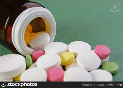 Scattered pills and a jar on a green background