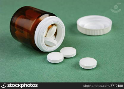 Scattered pills and a jar on a green background