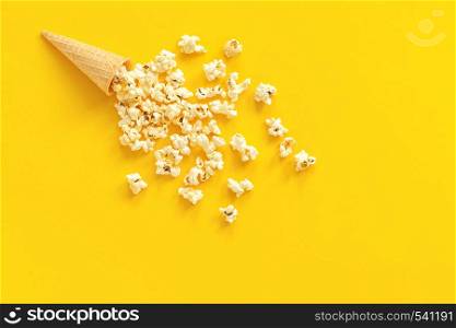 Scattered popcorn in ice cream waffle cone on yellow paper background. Top view Copy space Template for text or your design.. Scattered popcorn in ice cream waffle cone on yellow paper background. Top view Copy space Template for text or your design