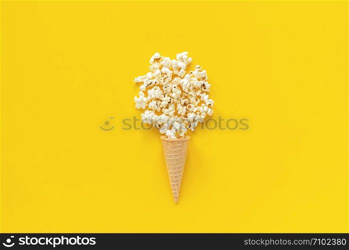 Scattered popcorn in ice cream waffle cone on yellow paper background. Top view Copy space Template for text or your design.. Scattered popcorn in ice cream waffle cone on yellow paper background. Top view Copy space Template for text or your design