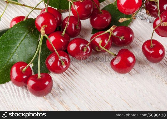 Scattered red sweet cherry and green leaves on a wooden background