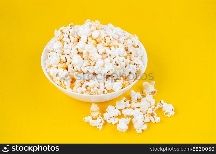 Scattered tasty cheese popcorn in white bowl isolated on yellow background. Flat lay, top view. Fast food, movie, cinema concept