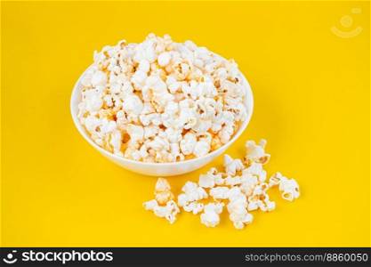 Scattered tasty cheese popcorn in white bowl isolated on yellow background. Flat lay, top view. Fast food, movie, cinema concept
