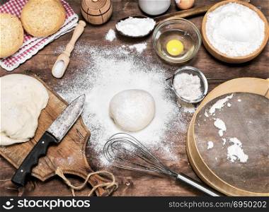 scattered wheat flour on the table, next to raw yeast dough and ingredients for bread making