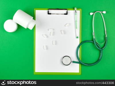 scattered white oval tablets from a plastic jar, stethoscope, medical background, top view