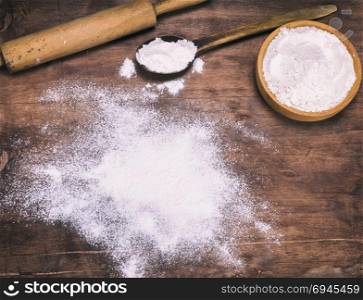 scattered white wheat flour on a brown wooden background, next to a wooden rolling pin