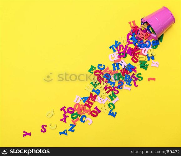 scattered wooden multicolored letters of the English alphabet from an iron bucket to a yellow background