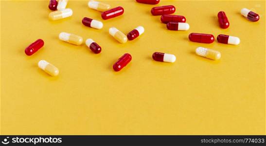 Scattered yellow and red drug capsules with active microgranules on a yellow background. Scattered yellow and red drug capsules with active microgranules