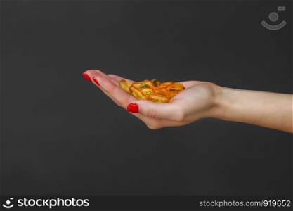 Scattering of transparent yellow pills. Handful of capsules in palm of hand, close-up, isolated on gray background. Capsules fish oil, omega 3. Healthy lifestyle, dietary nutritional supplements.. Scattering of transparent yellow pills. Handful of capsules in palm of hand, close-up, isolated on gray background.